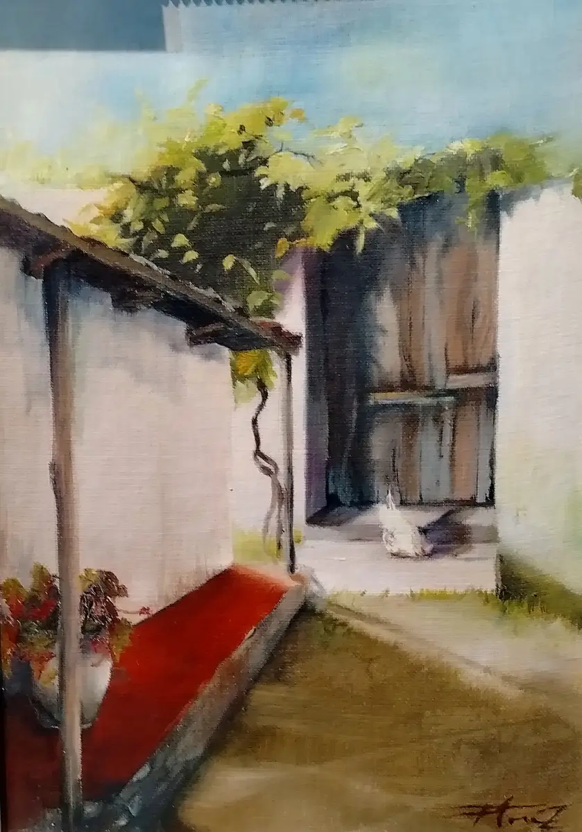 Esta pintura al óleo retrata un pasaje o callejón rústico, con paredes encaladas y un suelo de tierra. Un vibrante follaje verde se extiende por encima, mientras que un banco o saliente rojo añade un toque de color en primer plano, y un pequeño ave blanca se asoma junto a una puerta de madera al fondo. La composición evoca una escena tranquila y soleada de un entorno rural o tradicional.