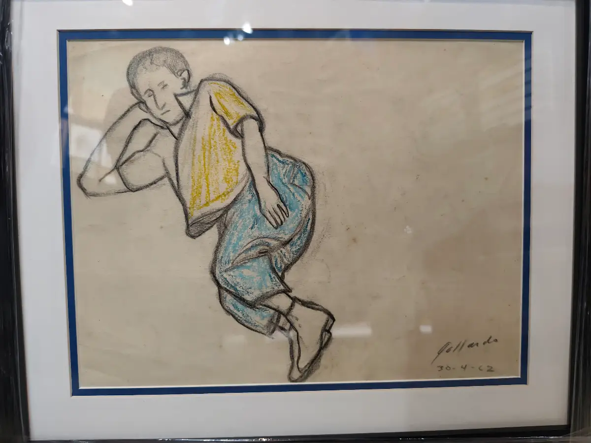 Un dibujo que representa a una figura masculina joven recostada, con la cabeza apoyada en un brazo, en una pose pensativa o melancólica. El artista utiliza trazos simples y expresivos en gris, realzados con toques de amarillo brillante para la camiseta y azul claro para los pantalones, sobre un fondo neutro. La composición sugiere un momento de introspección y descanso.