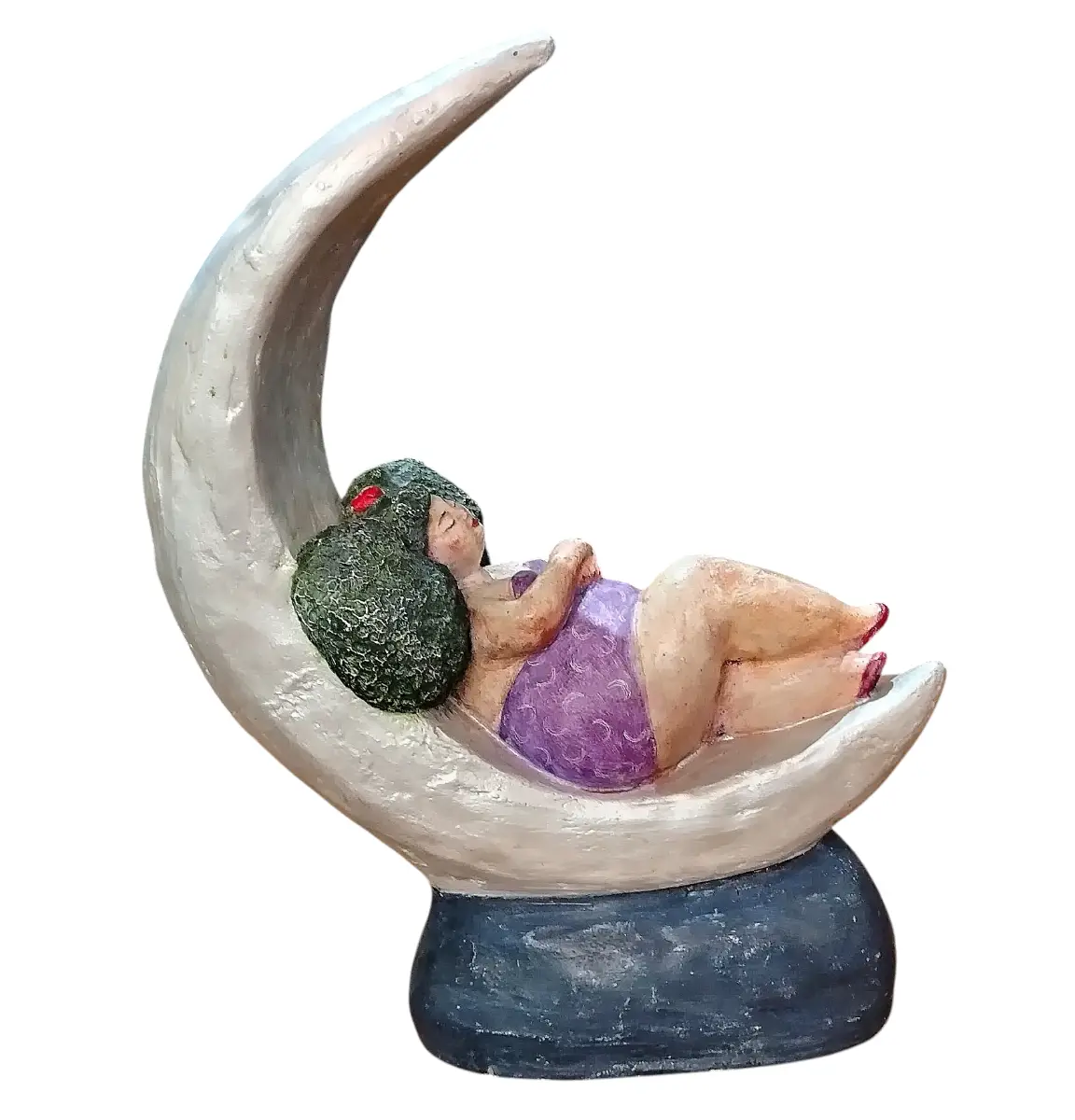 Esta escultura de cerámica retrata a una mujer serena y de figura completa, con cabello oscuro y texturizado, vestida de morado, durmiendo grácilmente sobre una brillante luna creciente plateada. El motivo celestial se asienta sobre una base texturizada de color azul oscuro, todo presentado sobre un fondo blanco y limpio. La obra emana una sensación de tranquilidad y paz onírica.